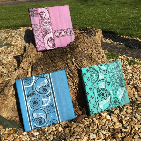 Three colourful custom painted canvases leant on tree stump