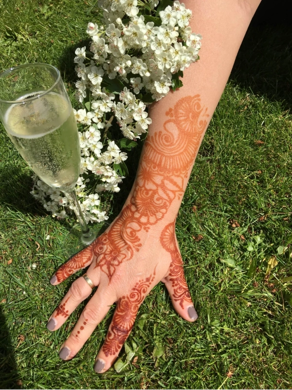 Henna on hand and forearm next to glass of procesco and flowers